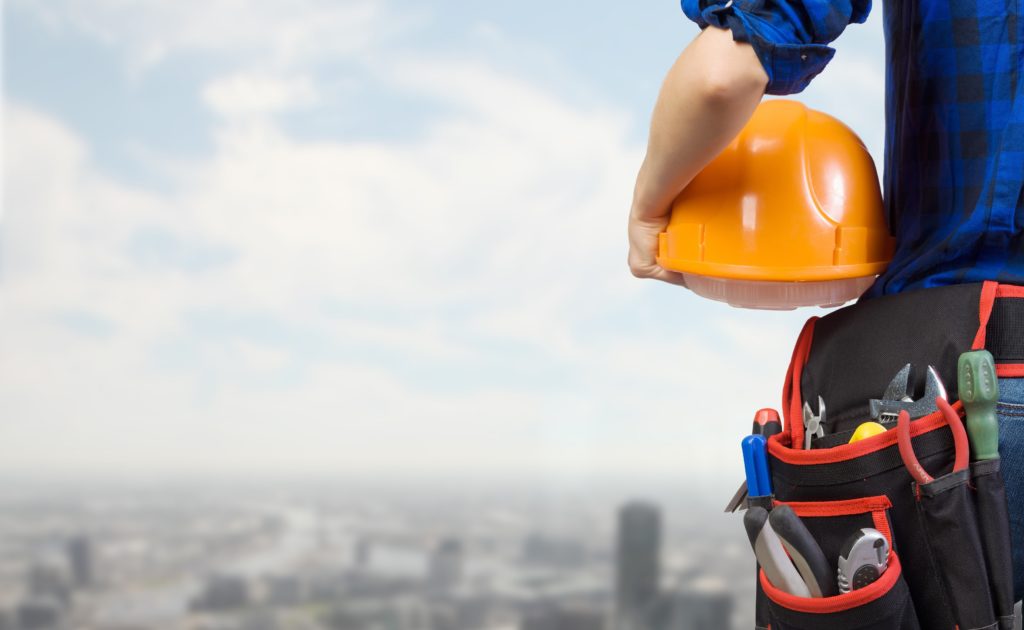 field technician looking out over a cityscape, holding a yellow hard hat