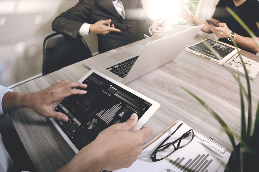 sales people around a desk having a meeting, looking at graphs on their tablets